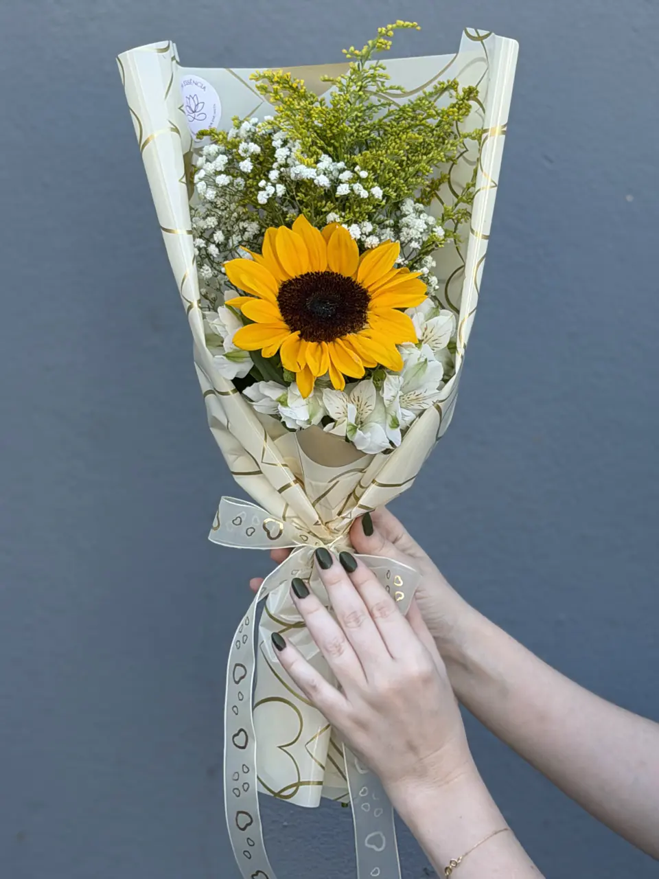 Mini buquê com um girassol e gypsophila sendo entregue em mãos